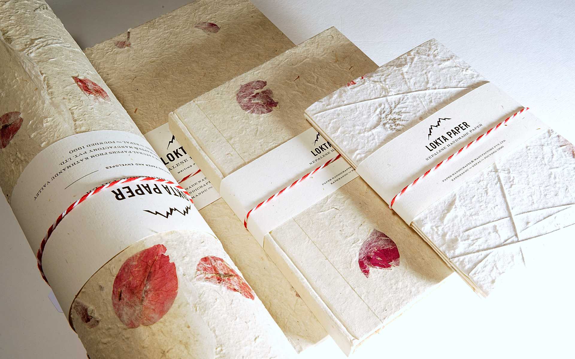 Abbildung einer Lokta-Papierkollektion mit eingeschossenen rötlichen Blüten. Das handgefertigte Papier stammt aus dem Himalaya in Nepal.