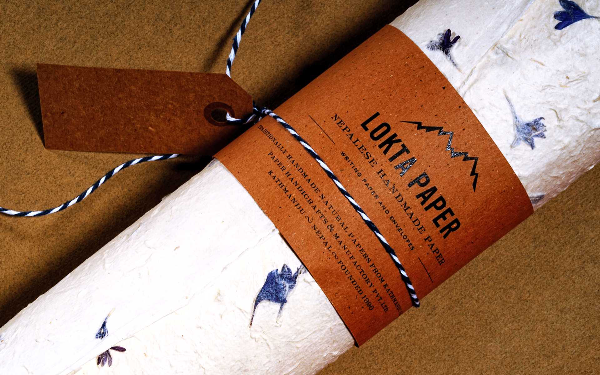 Abbildung von Geschenkpapier aus Lokta-Papier mit eingeschossenen violetten Blüten. Das handgefertigte Papier stammt aus Nepal.